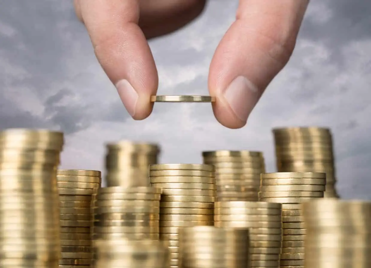 Hand holding and stacking gold coins in towers high